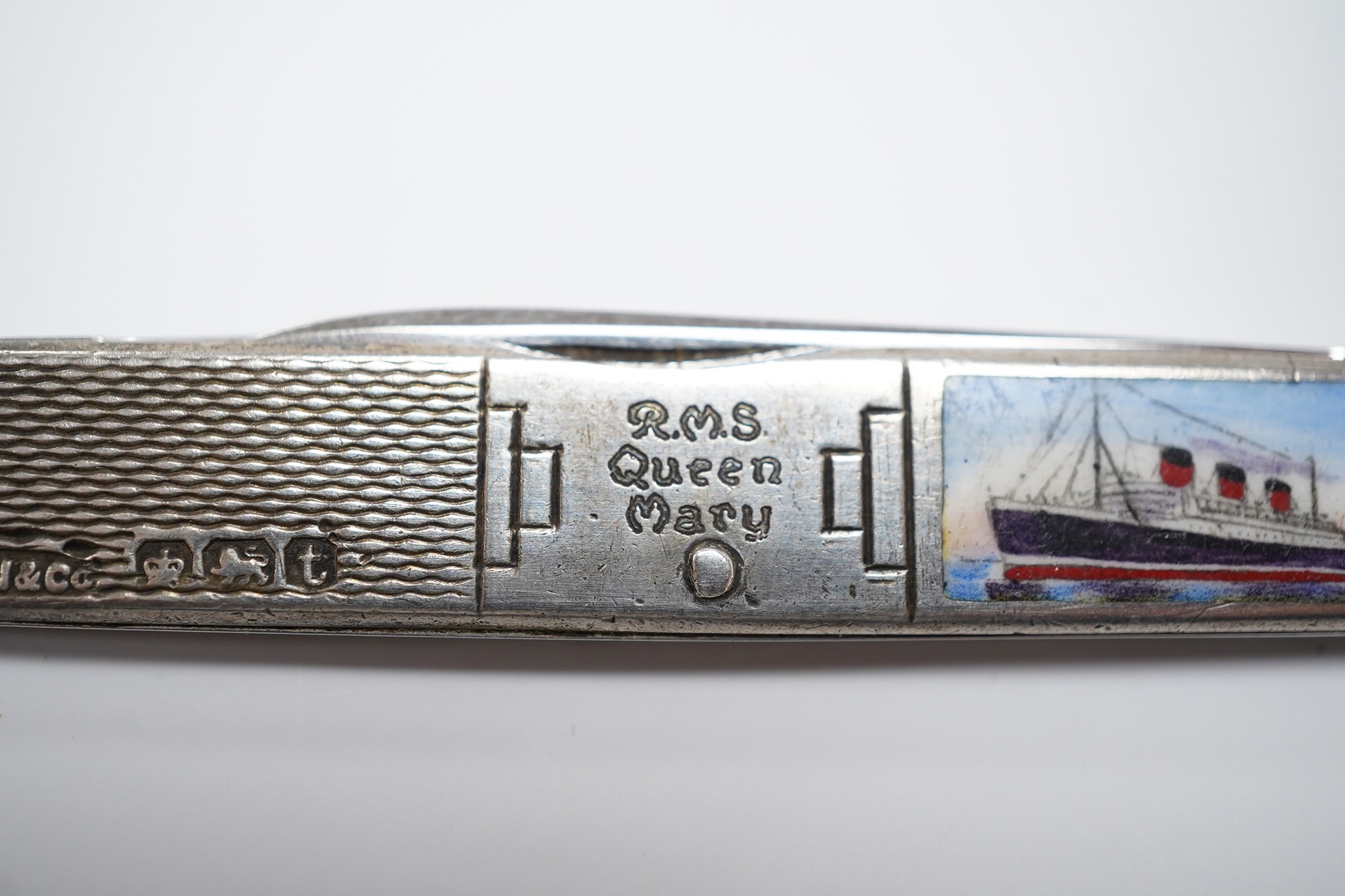 A George V engine turned silver and enamel pocket knife, decorated with R.M.S Queen Mary, the blades lifted by the handles, George Ibberson & Co, Sheffield, 1936, 76mm. Condition - poor to fair